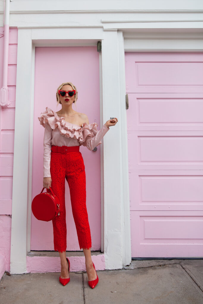 Valentines Day self care featured by top US life and style blog, Lombard and Fifth: image of a blonde woman wearing DressLily heart sunglasses, Roy Rogers red pants, a pink one shoulder ruffle blouse, Michka jeweled red pumps