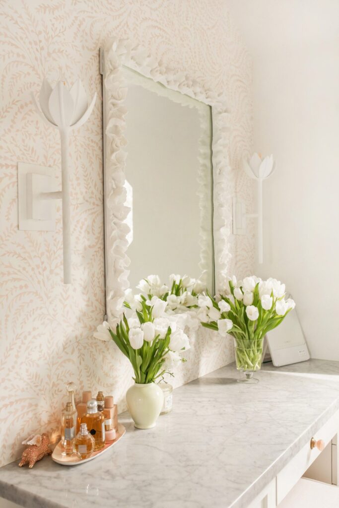 Bathroom vanity design décor update, with Serena & Lily priano pink wallpaper, rattan stool, white flower wall sconces and anthropologie zita drawer handles. By Veronica Levy, Lombard & Fifth.