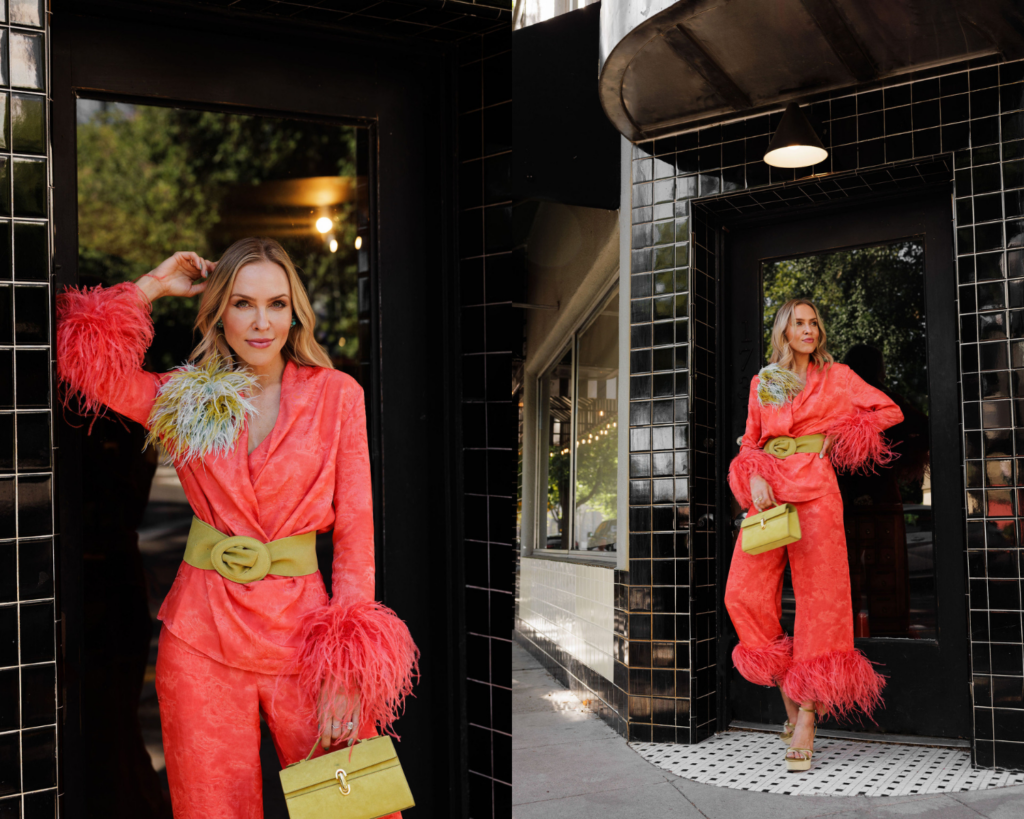 Coral satin suit styled with feather cuffs and a colorful feather brooch for a joyful statement look.