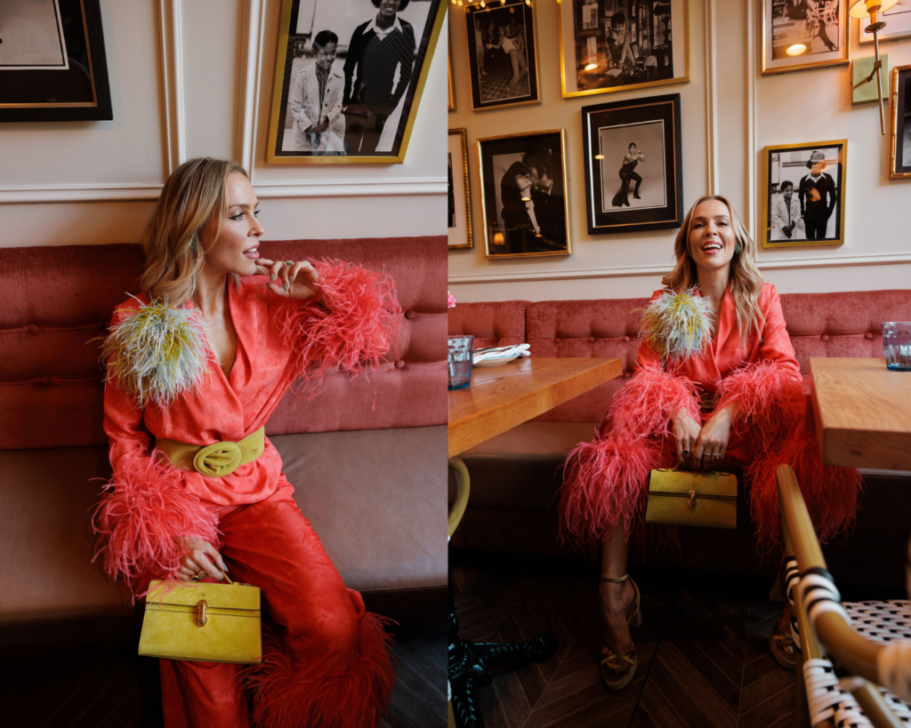 Coral satin suit styled with feather cuffs and a colorful feather brooch for a joyful statement look.