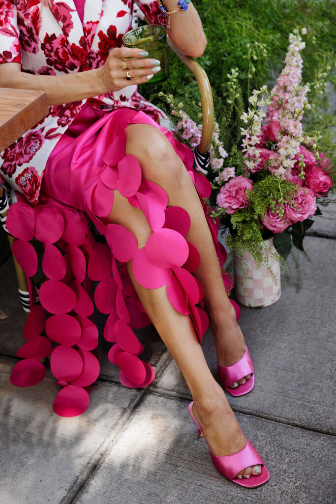 Close-up of colorful blue gemstone bracelets paired with a bright pink floral outfit and bouquet of flowers.