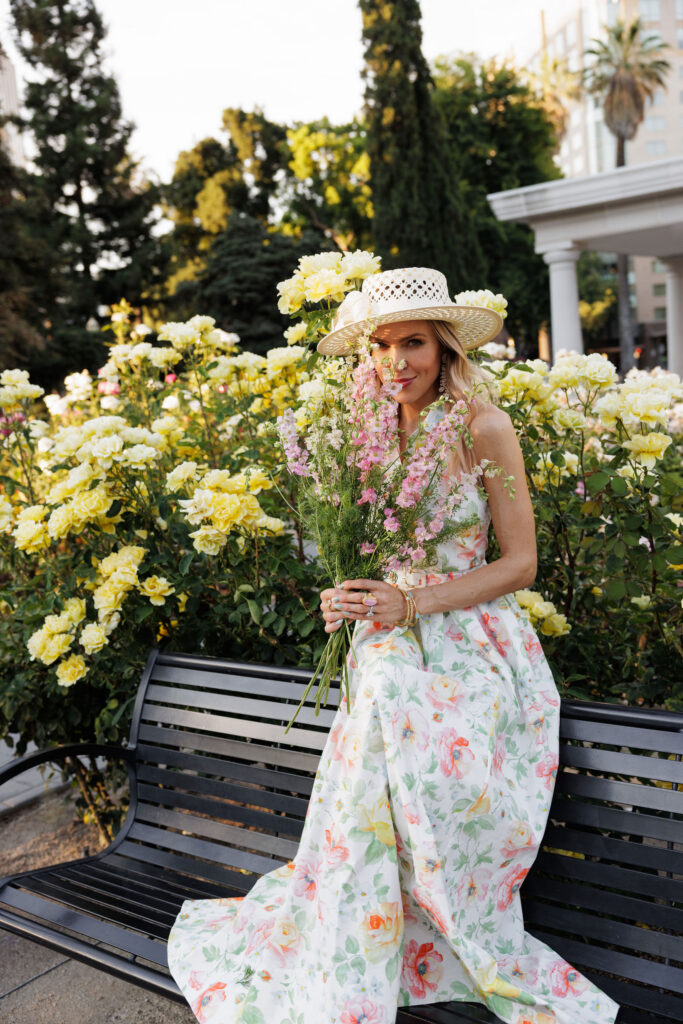 Woman in a floral Needle & Thread dress holding fresh pink flowers in a garden