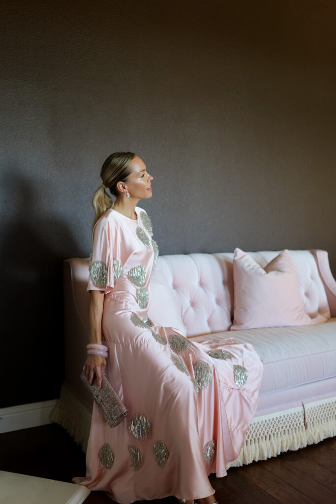 Editorial fashion photo of a woman styling a soft ballet pink satin dress with silver embellishments, reading a fashion magazine on a blush sofa.