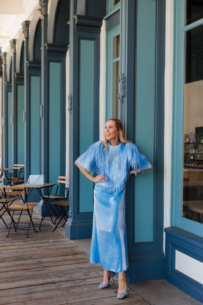 Editorial monochromatic blue outfit featuring a shimmering fringe cape over a satin blue maxi dress with sparkling blue heels.