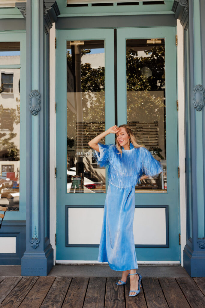 Light blue satin dress with metallic fringe overlay and matching blue heels styled for an editorial summer fashion look.