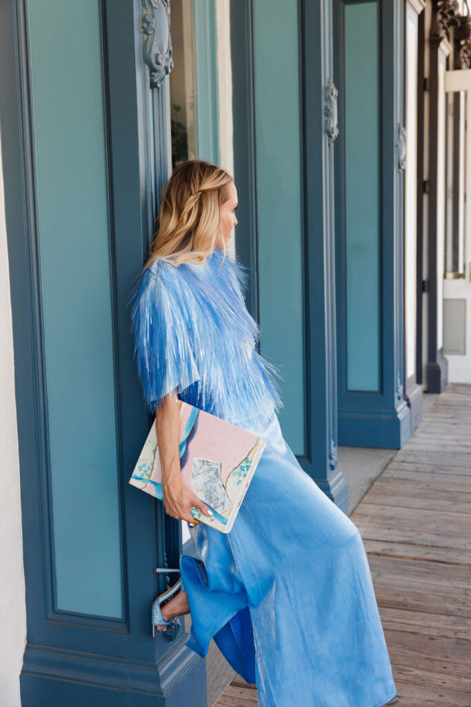 Light blue satin maxi dress with fringe cape top and blue embellished sandals styled in a monochromatic blue outfit.